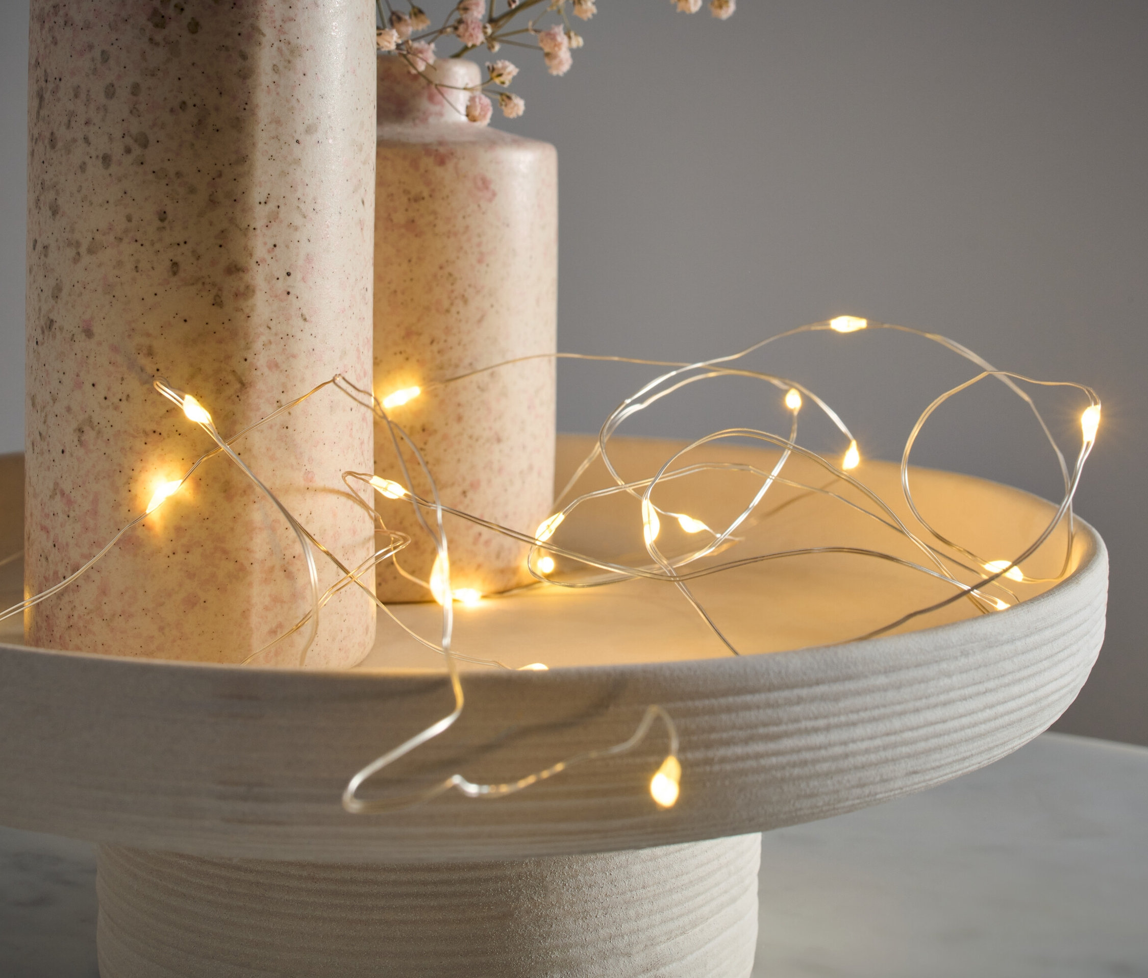 Łańcuch świetlny z mikrodiodami LED, krople, leży na ozdobnej tacy obok dwóch wazonów.