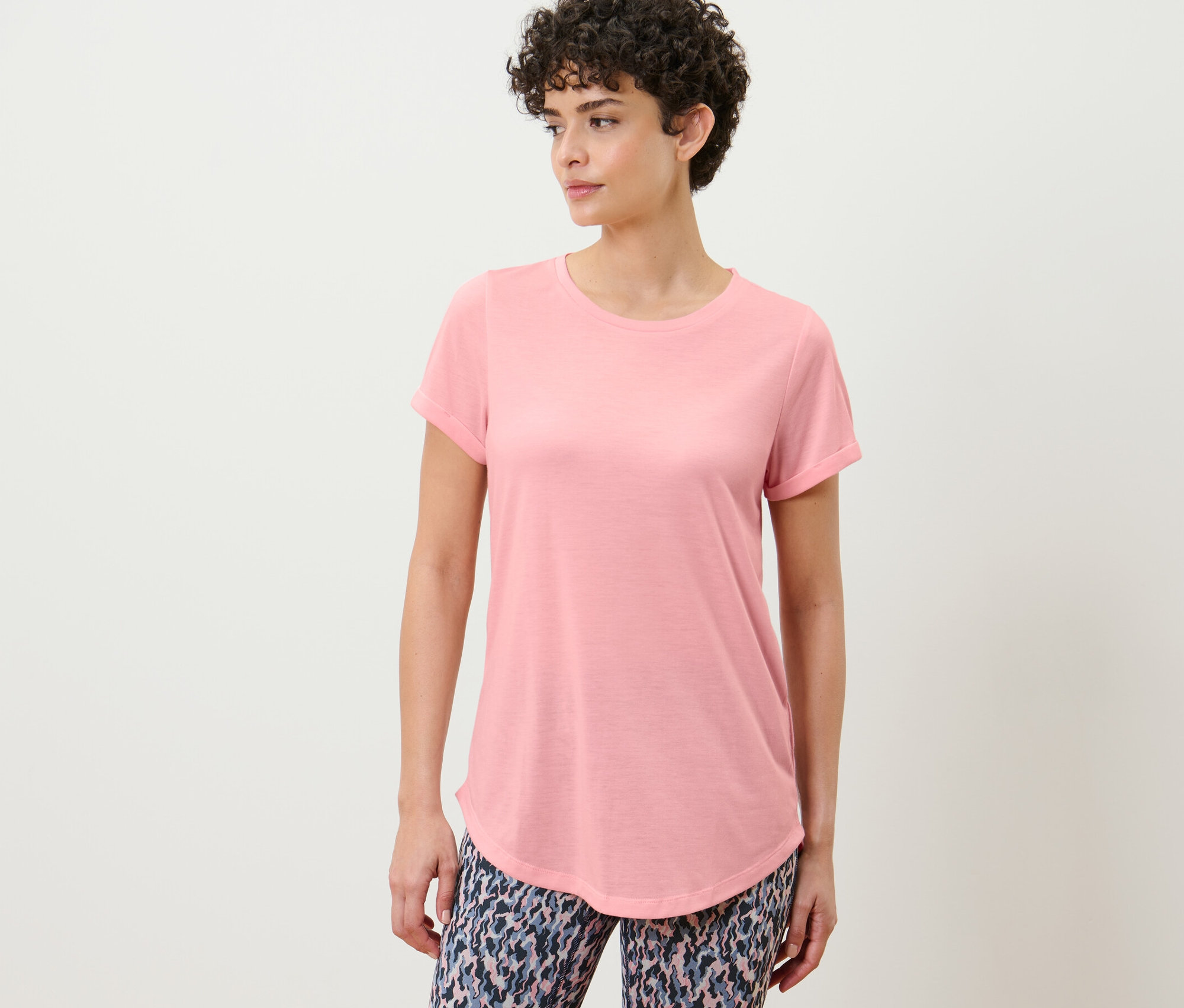 Kobieta pozuje w długiej koszulce, bladoróżowej.