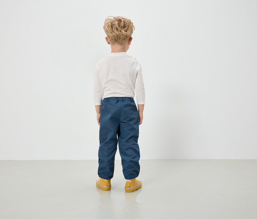 Chłopiec w niebieskich spodniach i żółtych butach stoi tyłem do kamery.