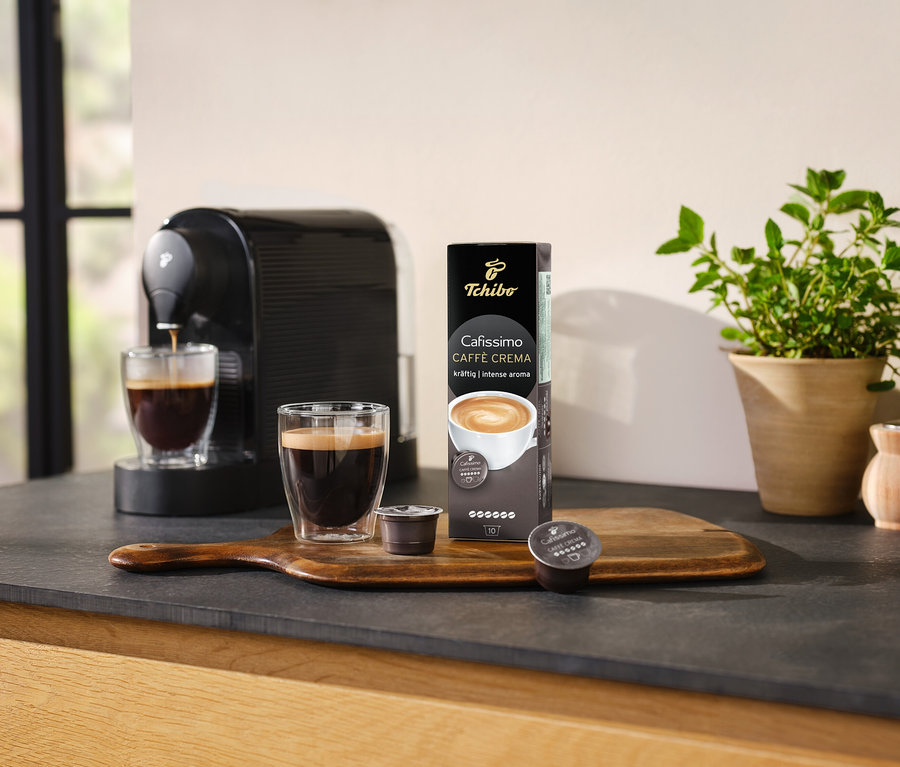 Ekspres do kawy przygotowuje kawę do szklanki obok opakowania Cafissimo Caffè Crema Intense Aroma – 10 kapsułek.