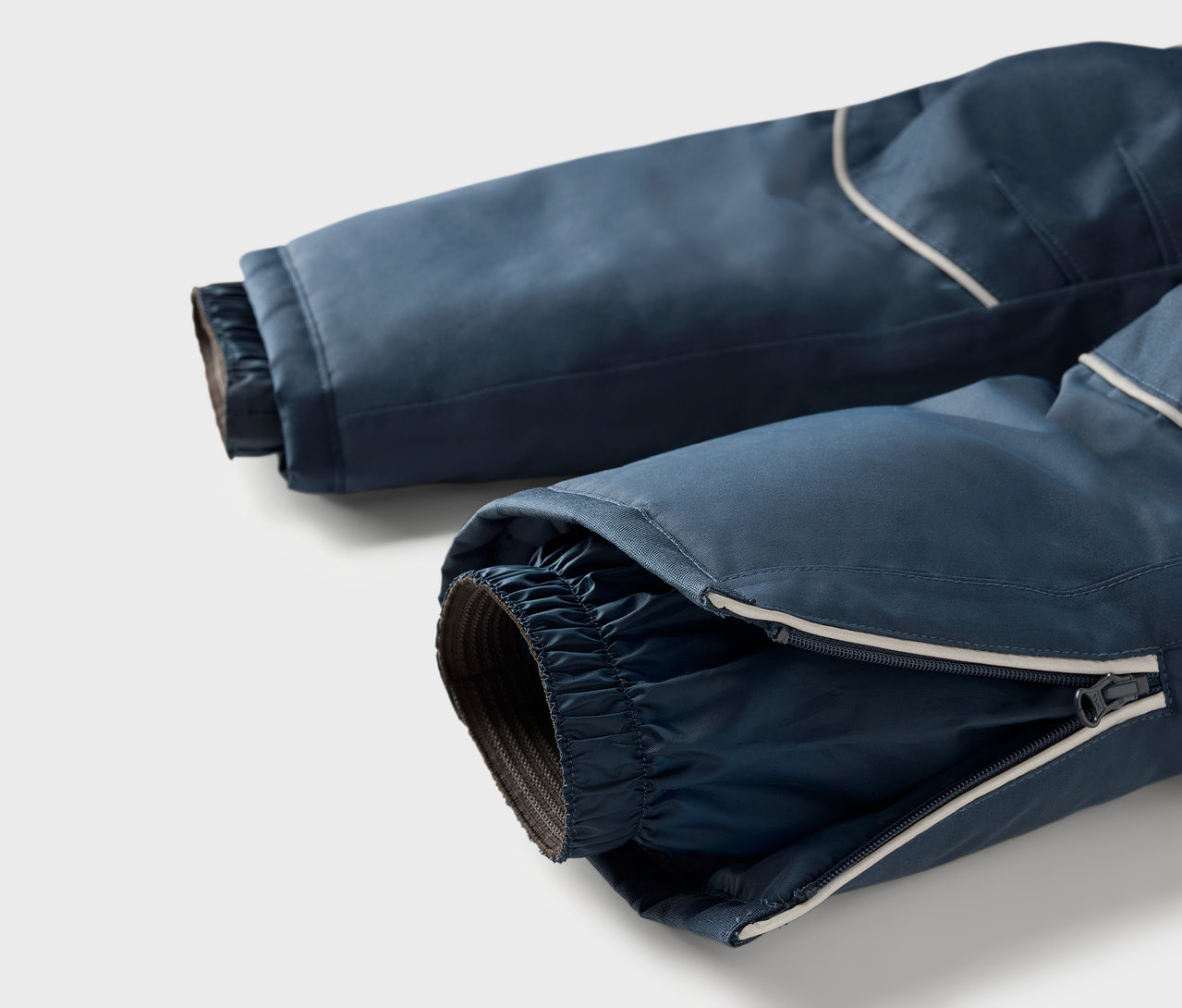 Szczegół granatowych spodni narciarskich z zamkiem błyskawicznym na nogawce i odblaskowym paskiem.