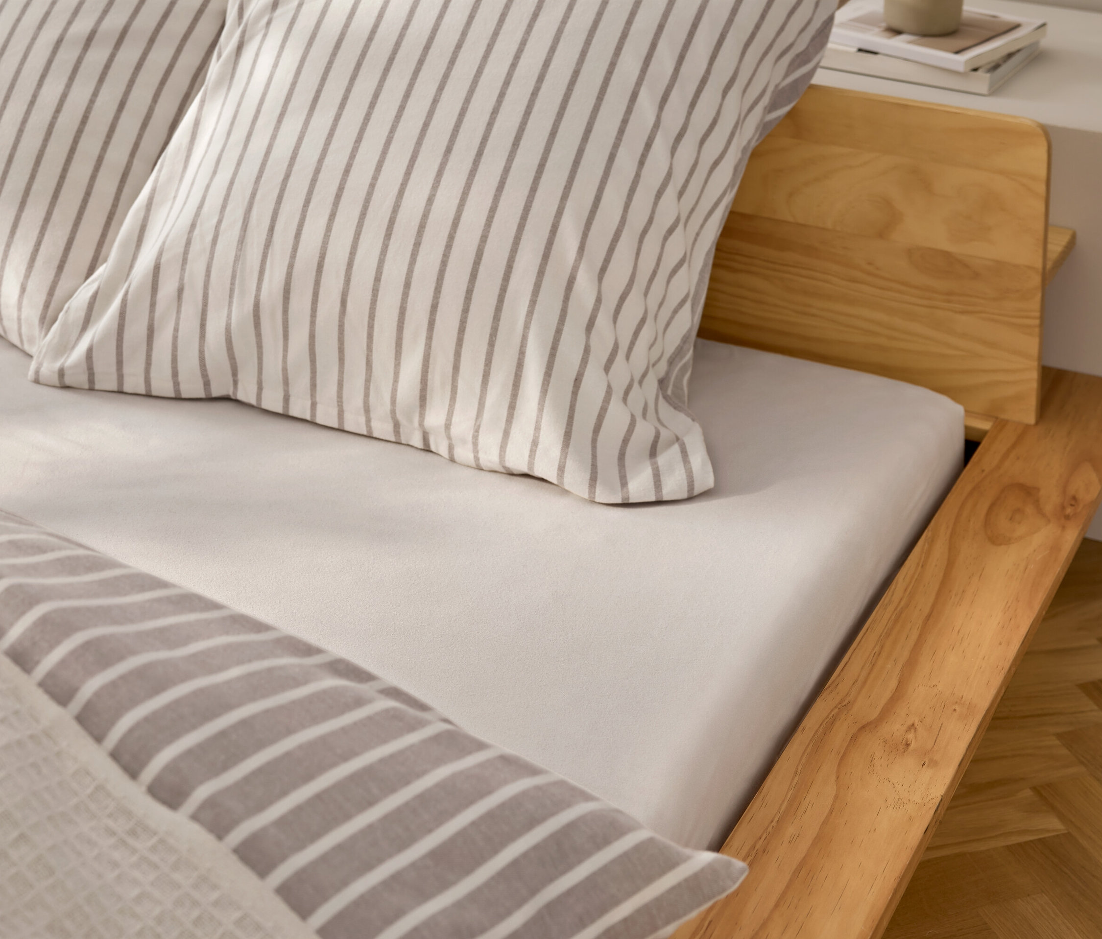 Szczegółowy widok łóżka z białym prześcieradłem i poduszkami w szare paski.