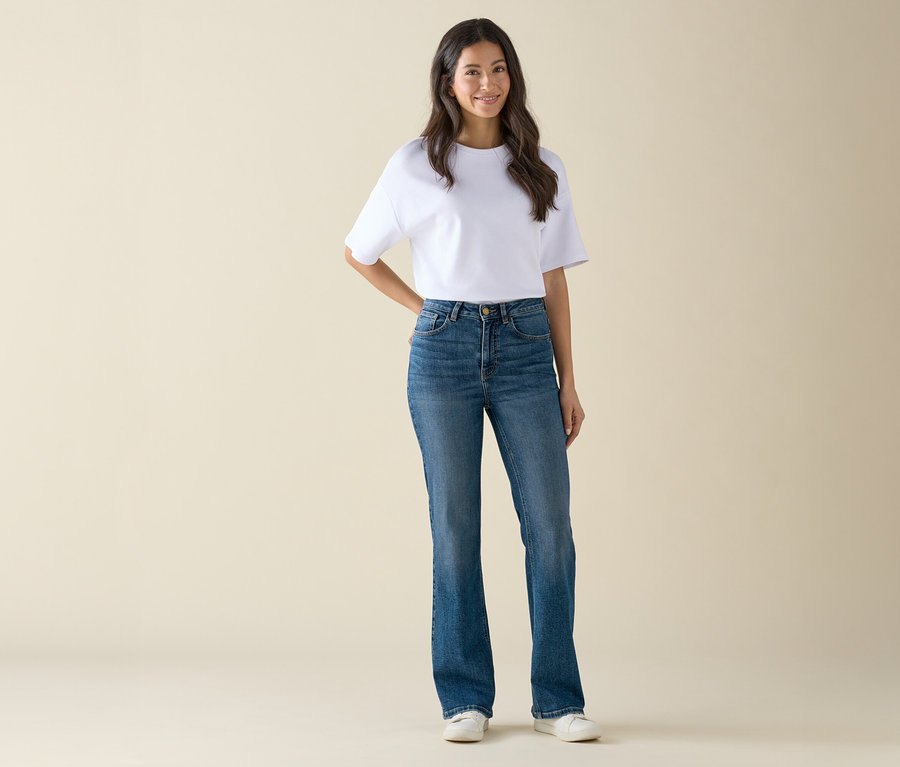 Kobieta w białej koszulce i niebieskich dżinsach stoi i pozuje.