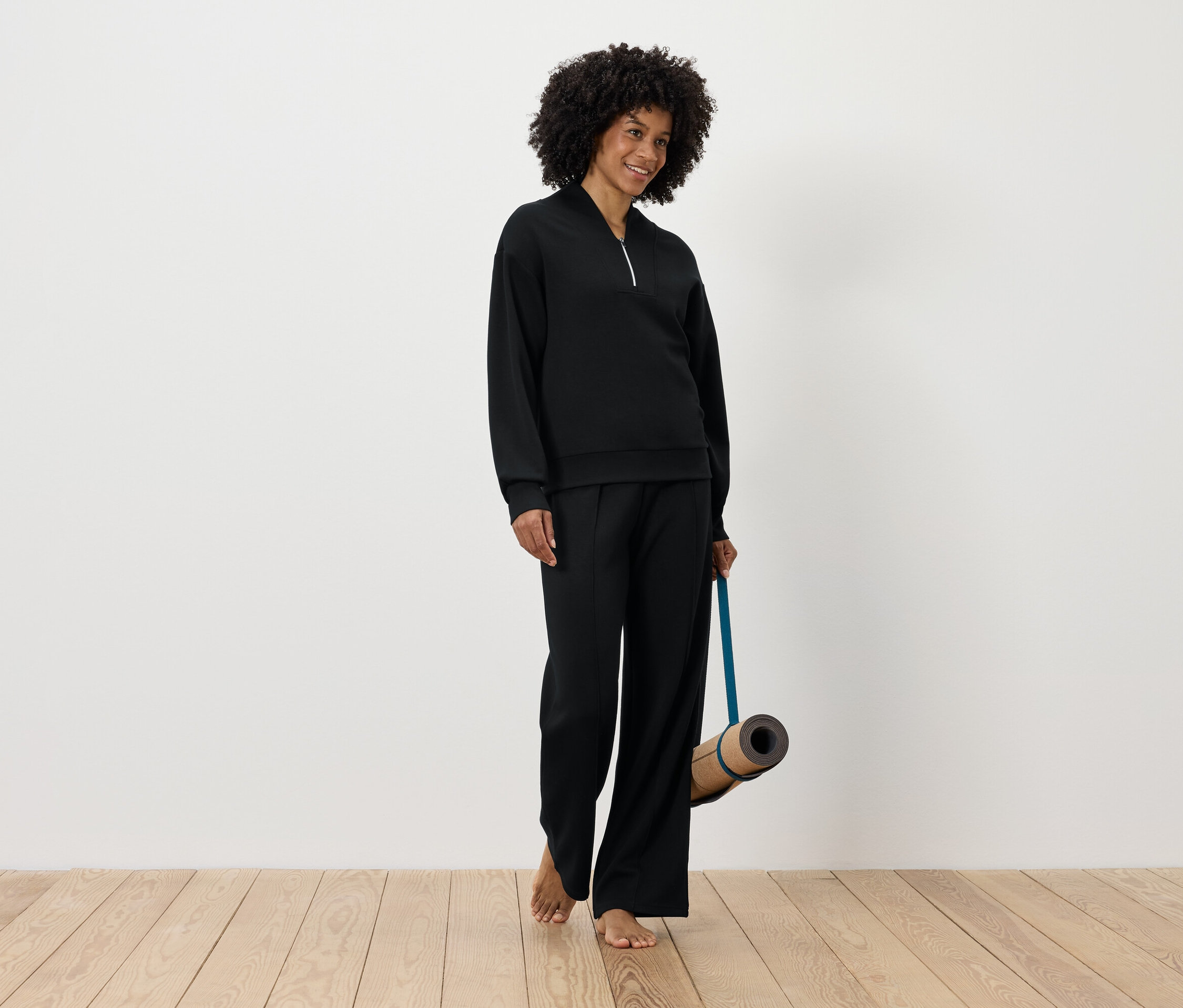 Kobieta w czarnym stroju sportowym trzyma matę do jogi.