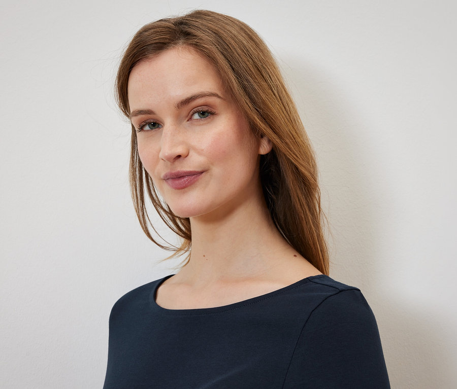 Portret kobiety z długimi brązowymi włosami i niebieskimi oczami, ubranej w granatową koszulkę.