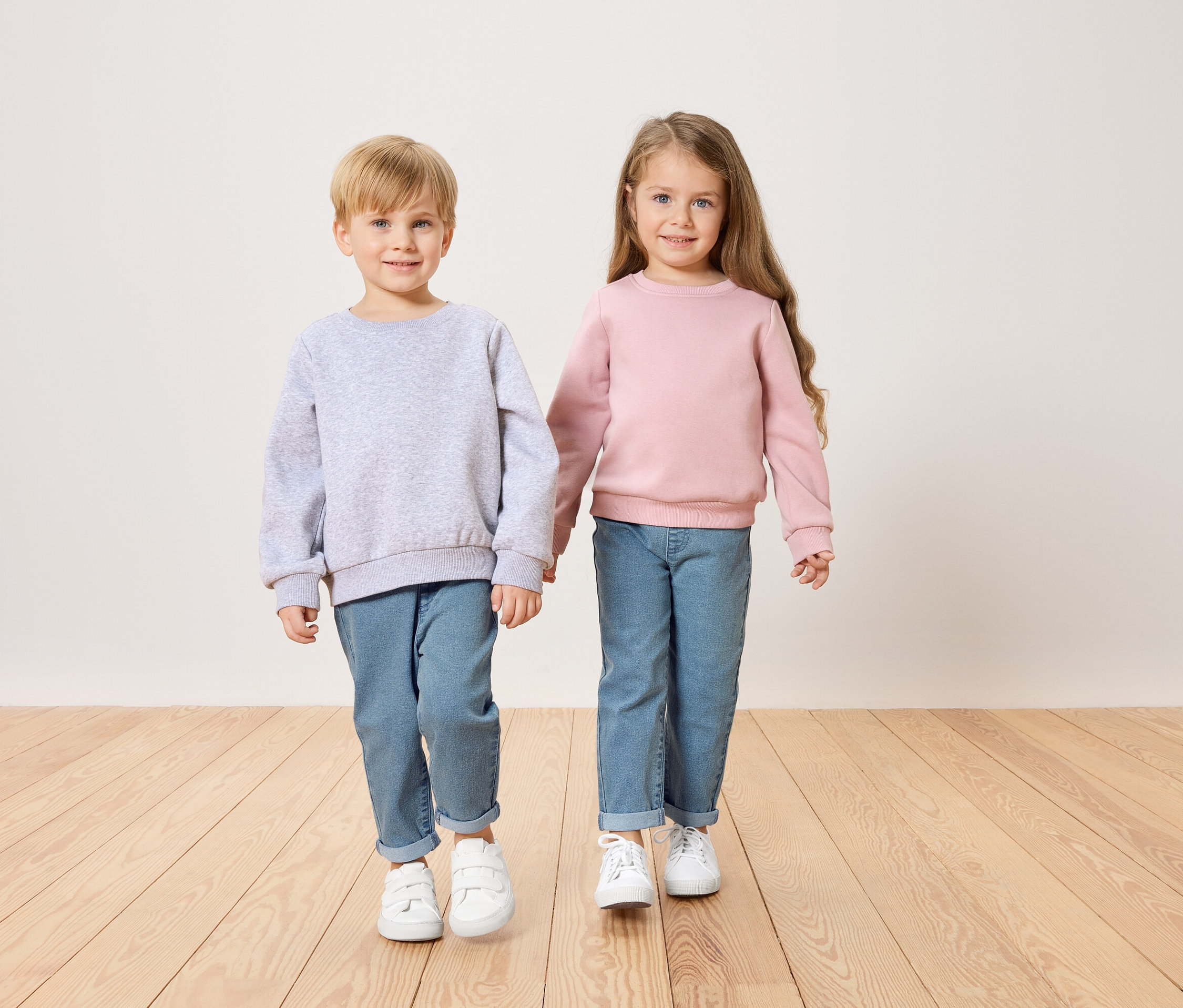 Chłopiec w szarej bluzie i dziewczynka w różowej bluzie trzymają się za ręce.