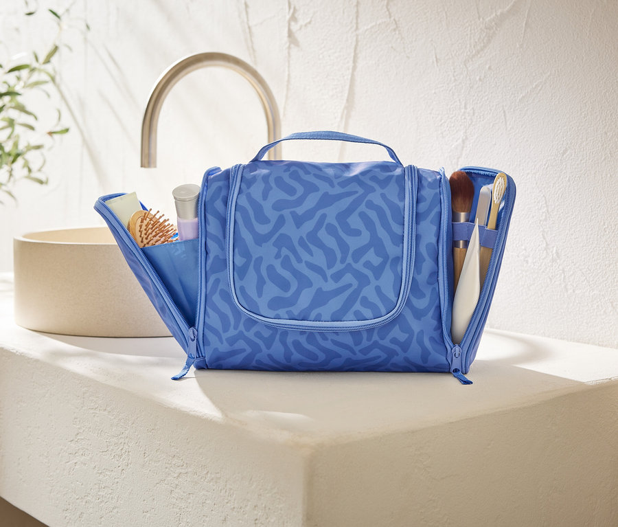 Otwarta, niebieska kosmetyczka z abstrakcyjnym wzorem stoi na białym blacie w łazience.