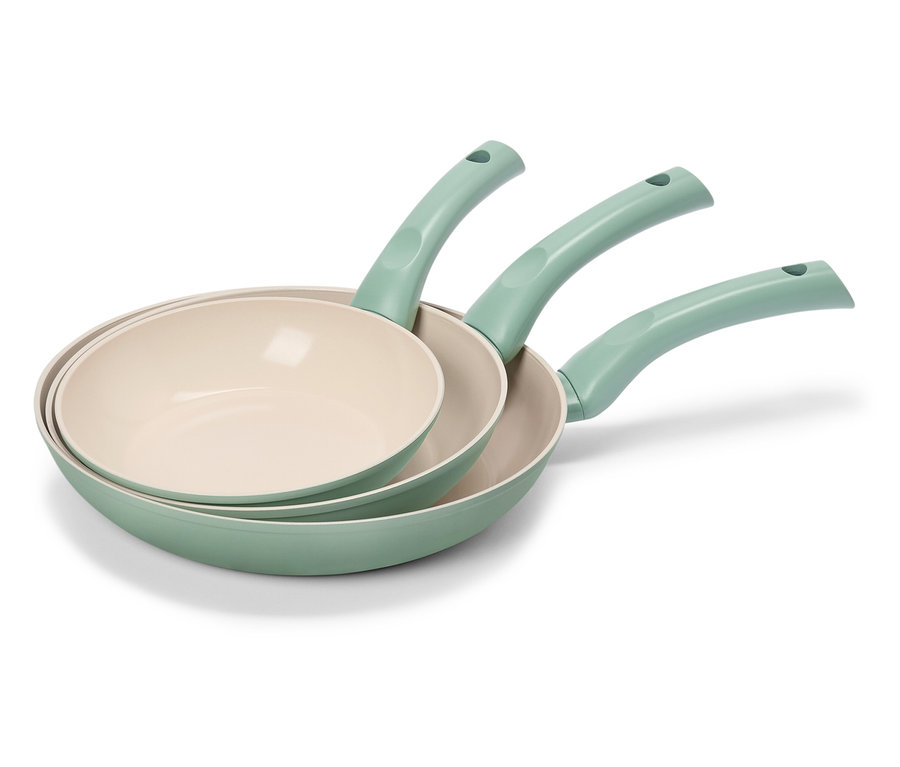 Trzy zielone patelnie z kremowymi powierzchniami wewnętrznymi są ułożone w stos.