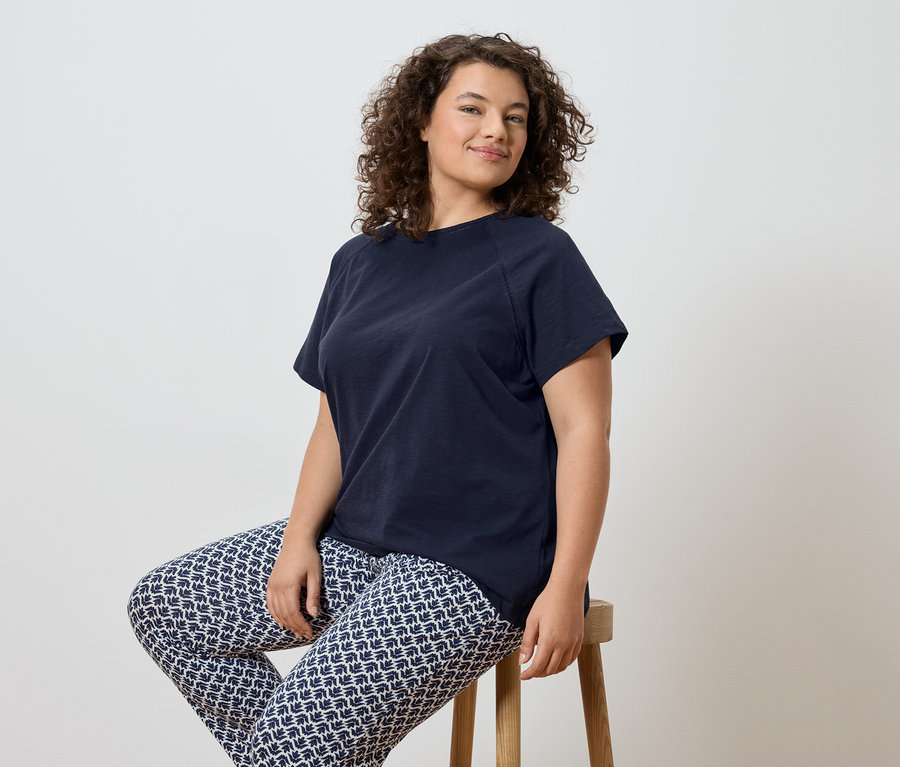 Kobieta o kręconych włosach siedzi na stołku, ubrana w granatowy T-shirt i wzorzyste legginsy.
