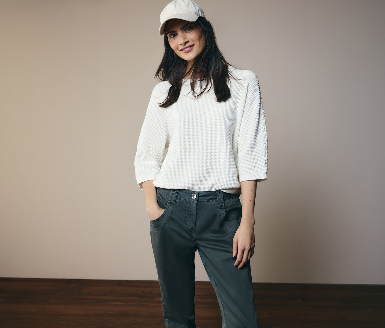 Kobieta w białej bluzce i czapce pozuje w spodniach CECIL „Scarlett” z rękami w kieszeniach.