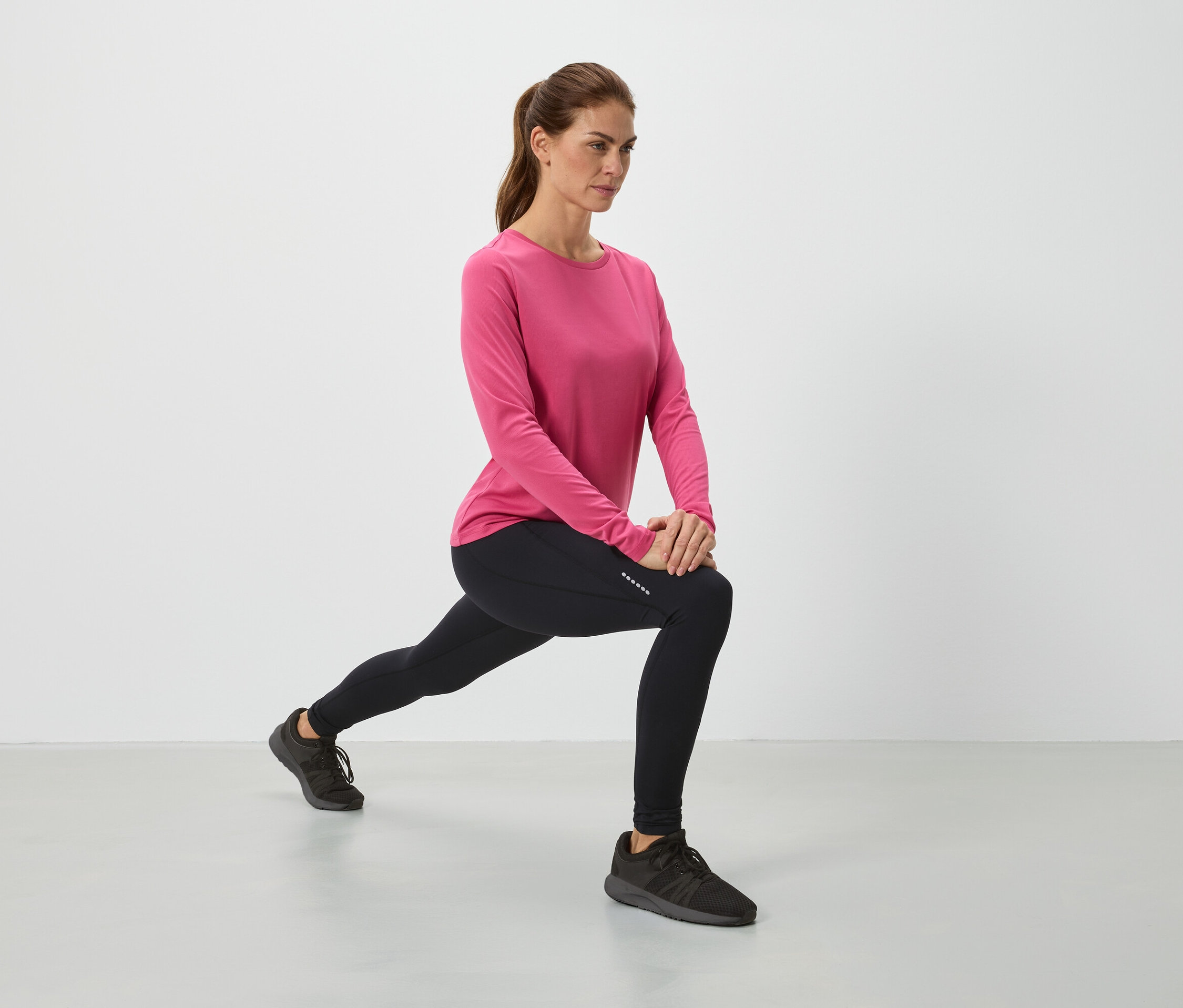 Kobieta w różowej bluzce i czarnych legginsach robi rozciąganie.