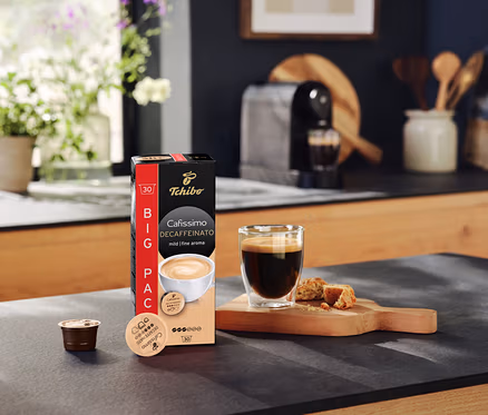 Na blacie kuchennym stoi opakowanie kapsułek Cafissimo Decaffeinato, filiżanka kawy i kapsułka.