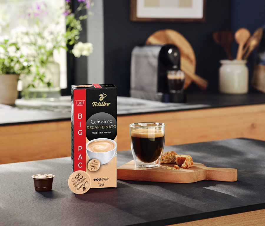 Na blacie kuchennym stoi opakowanie kapsułek Cafissimo Decaffeinato, filiżanka kawy i kapsułka.