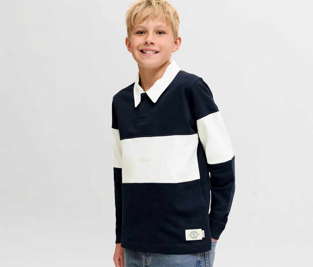 Uśmiechnięty blond chłopiec w granatowo-białym, pasiastym swetrze polo Jack&Jones z białym kołnierzykiem.
