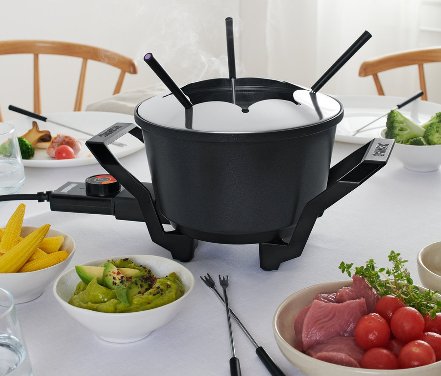 Na stole stoi fondue z widelcami i składnikami.