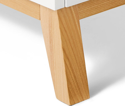 Detal białej komody z nogami z jasnego drewna.