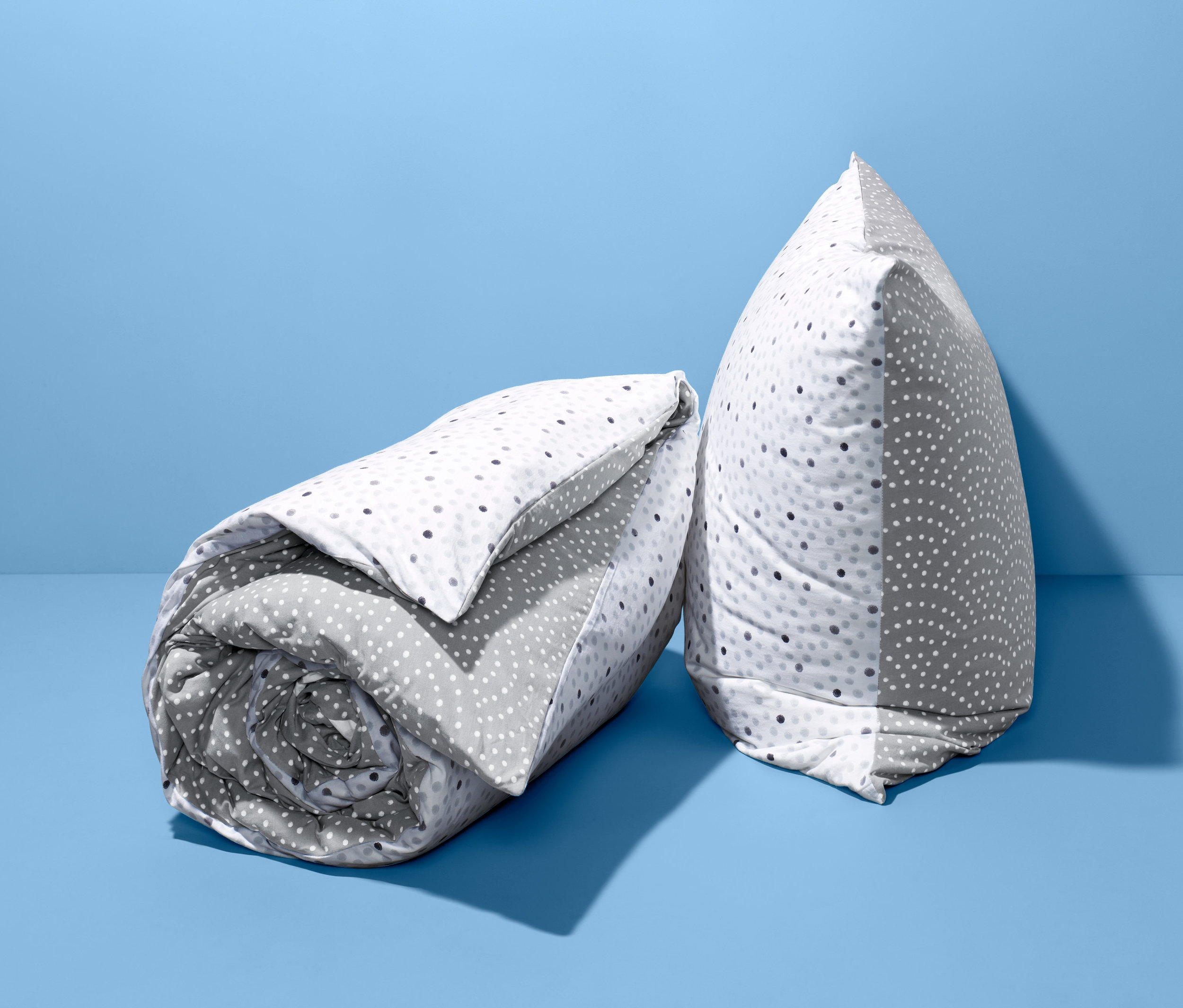 Zrolowany i złożony dwustronny komplet pościeli z dżerseju w standardowym rozmiarze w kropki na niebieskim tle.