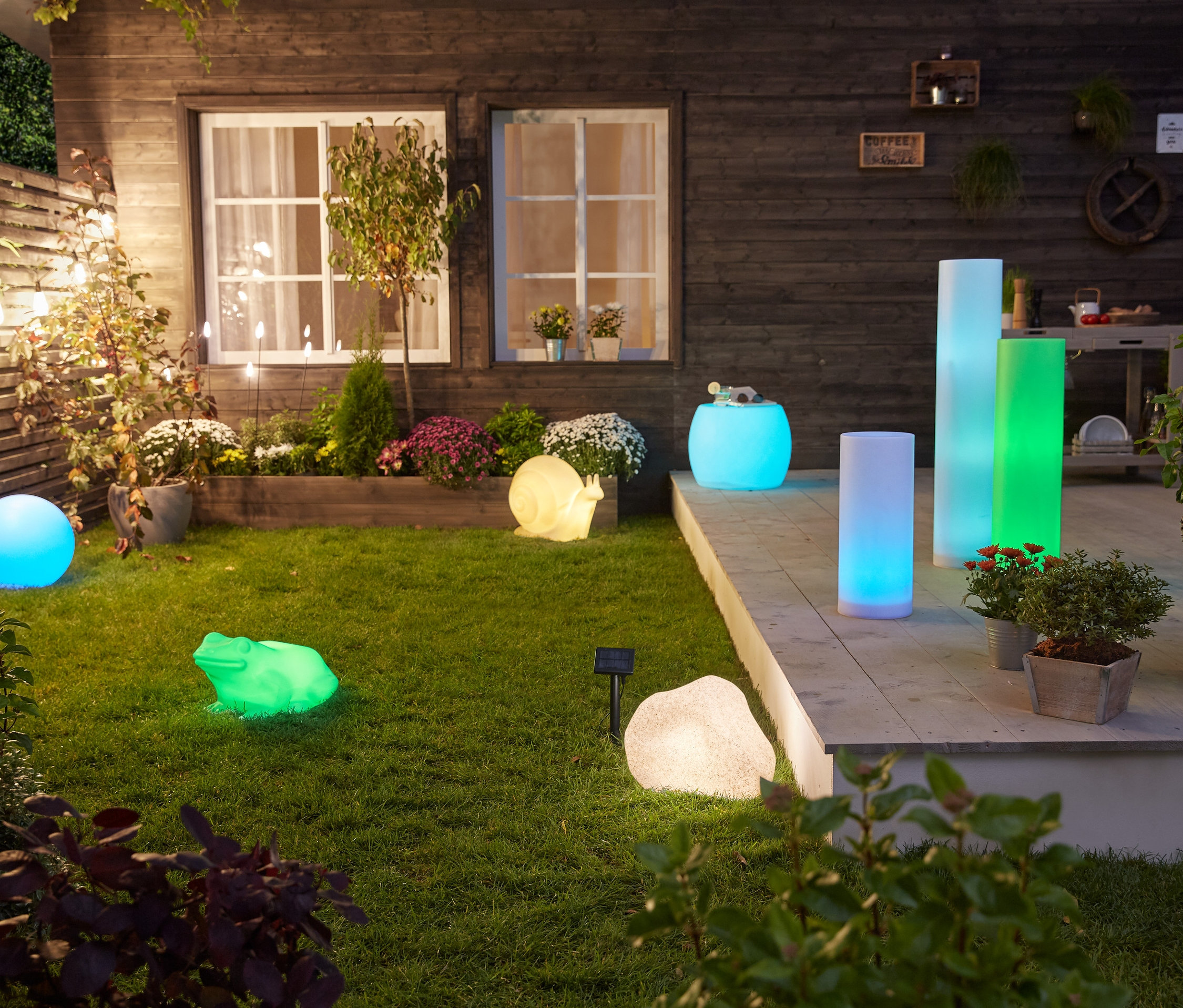 Na trawniku i tarasie stoją lampy solarne: żaba, ślimak, kamień, kula, 5 szt. pałeczek solarnych, słupek 50 cm, 75 cm, 100 cm i stolik.