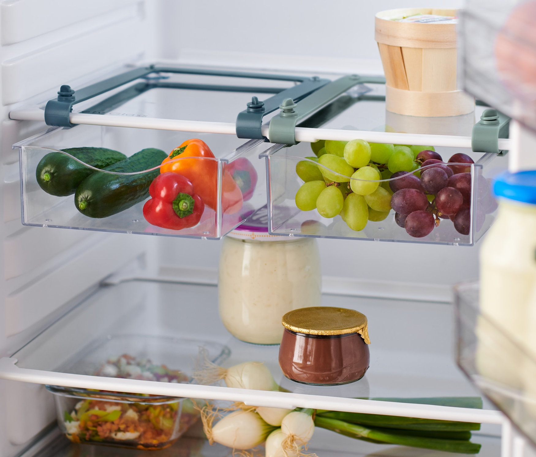 Widok do lodówki z dwoma wysuwanymi pojemnikami. W jednym są ogórki i papryka, w drugim zielone i czerwone winogrona.