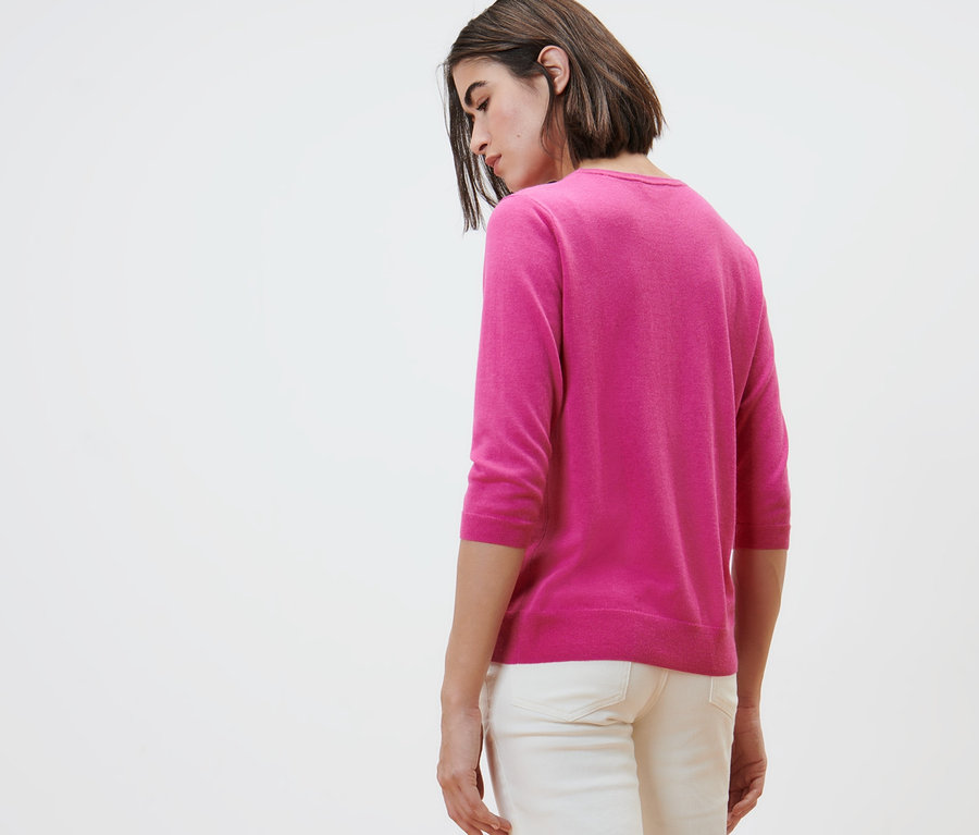 Kobieta pozuje w różowym swetrze dzianinowym o drobnym splocie z jedwabiem i białych spodniach.