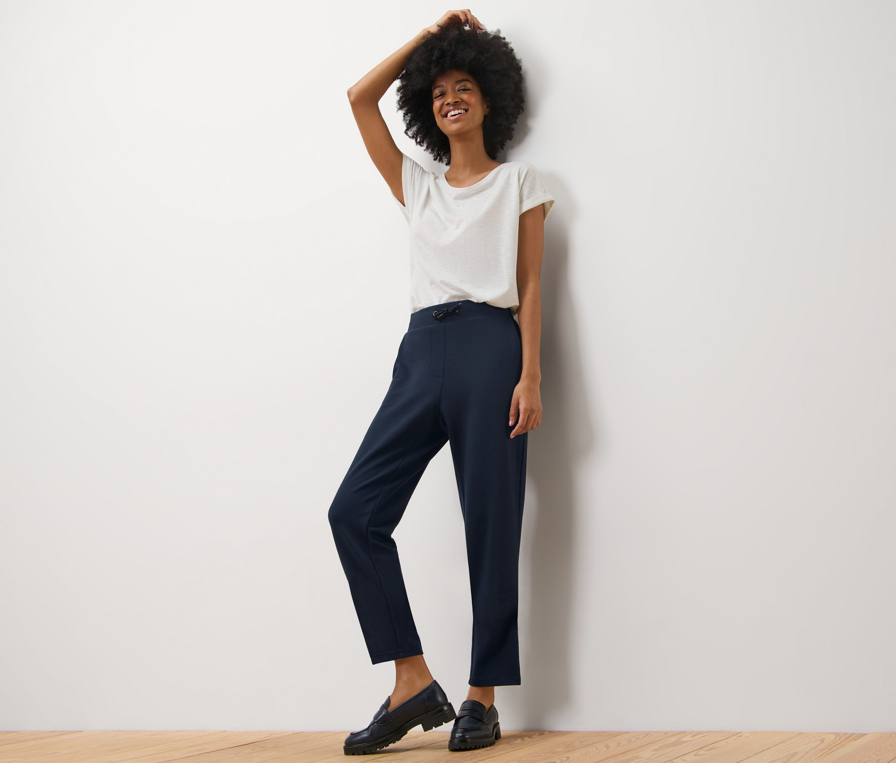 Kobieta pozuje w spodniach dresowych i białym T-shircie.