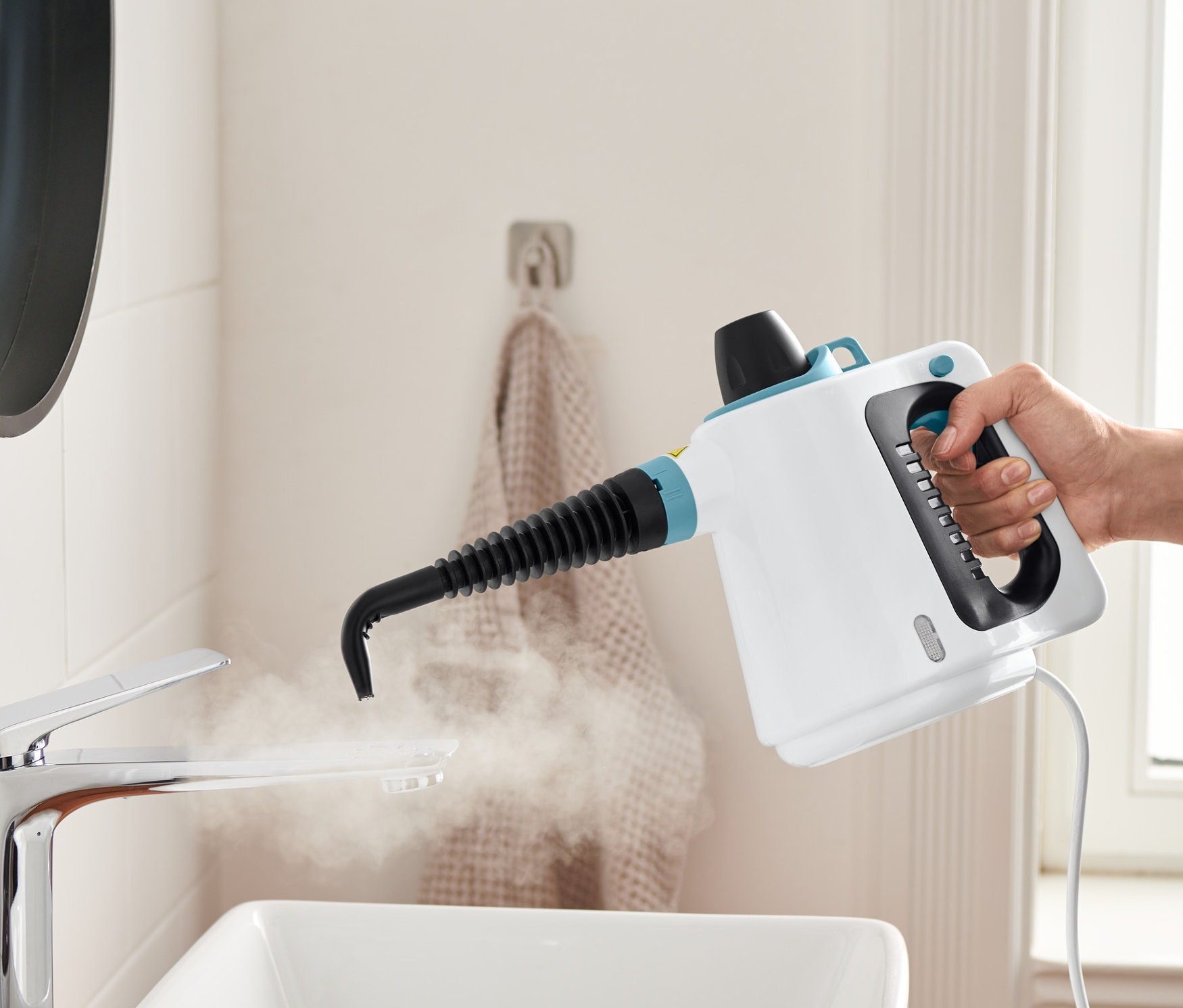 Ręka trzyma myjkę parową i czyści nią umywalkę.
