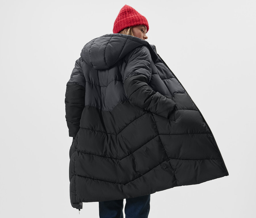 Kobieta ma na sobie płaszcz pikowany z kapturem i czerwoną czapkę.