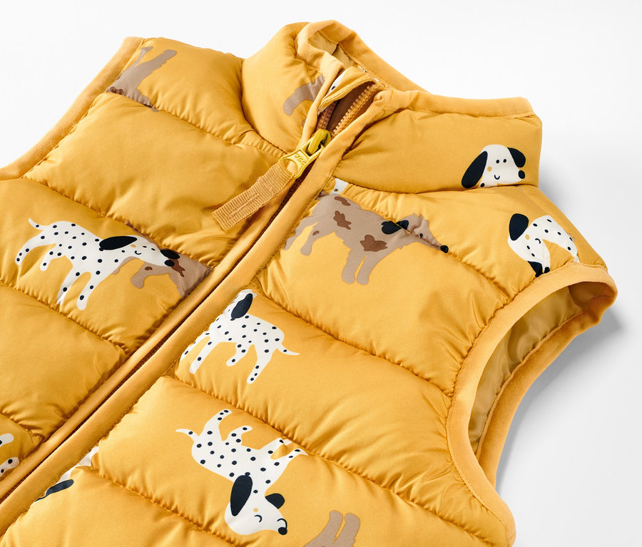 Zbliżenie na żółtą, pikowaną kamizelkę dziecięcą z nadrukiem psów.