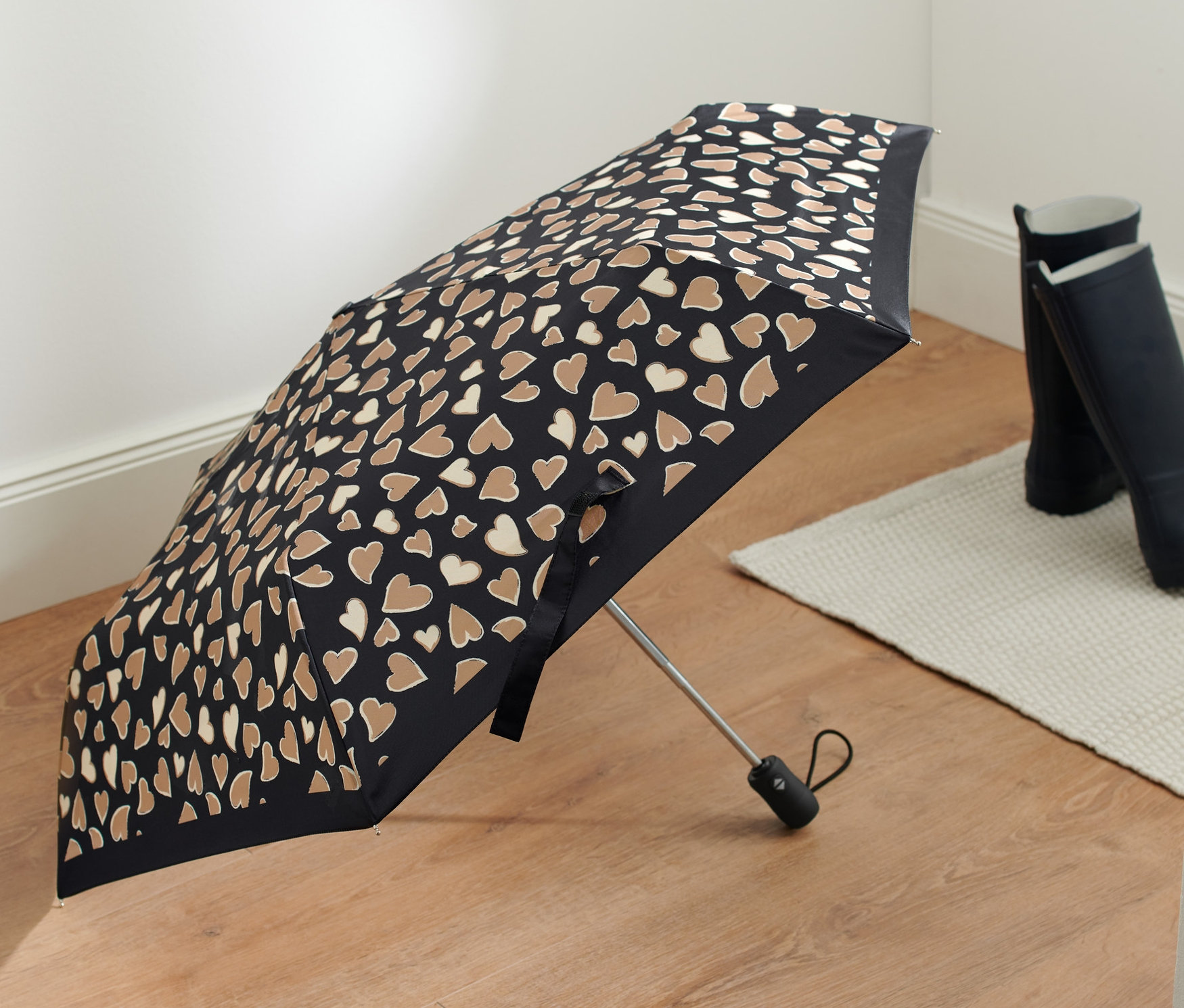 Otwarty, czarny kieszonkowy parasol automatyczny w brązowe serca leży na podłodze.
