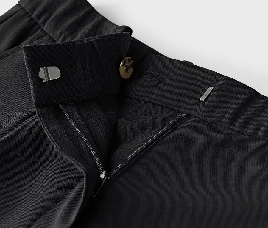 Zbliżenie na czarne spodnie materiałowe z zamkiem błyskawicznym i guzikiem.