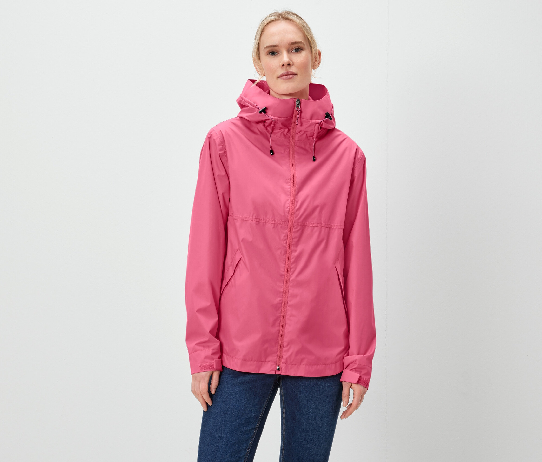Kobieta ma na sobie różową kurtkę z kapturem i niebieskie dżinsy.