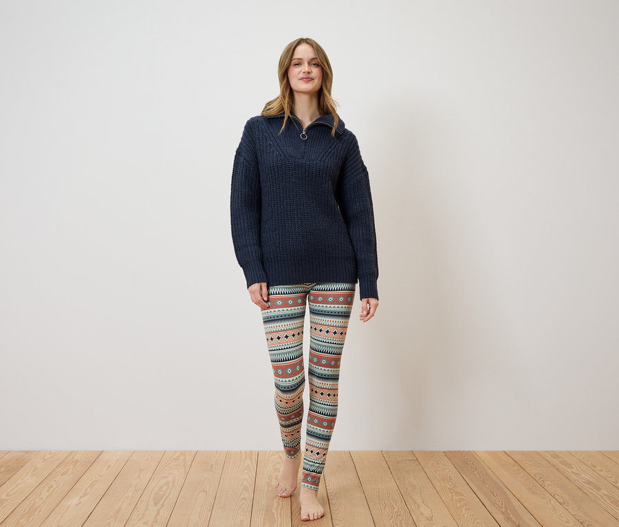 Kobieta stoi, ubrana w granatowy sweter i wzorzyste legginsy.