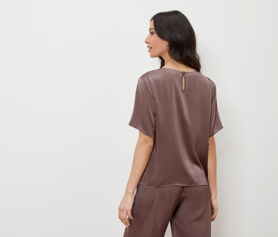 Kobieta w brązowej satynowej bluzce i spodniach, patrząca w lewo.