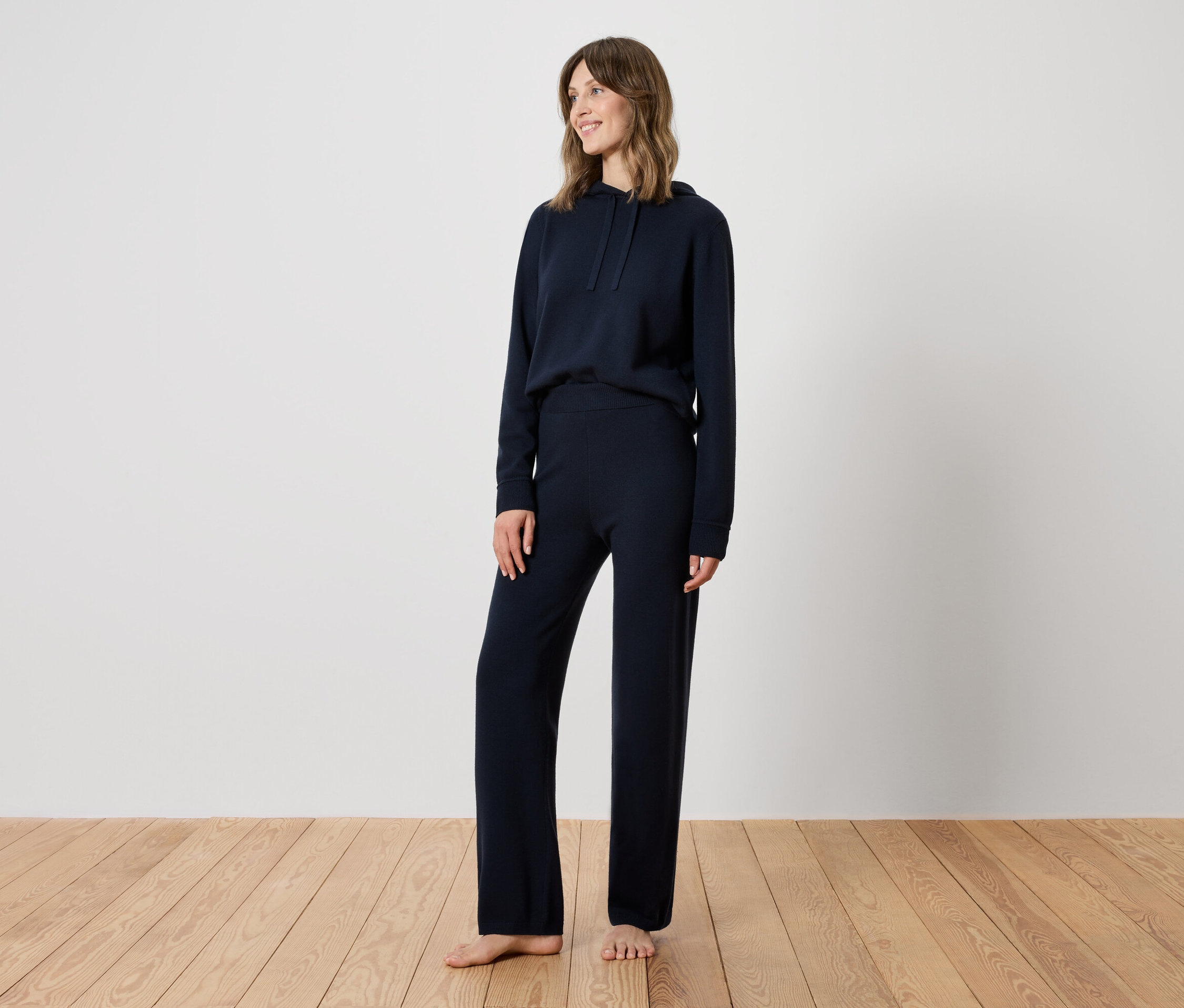 Kobieta stoi na drewnianej podłodze, ubrana w granatowy dres.