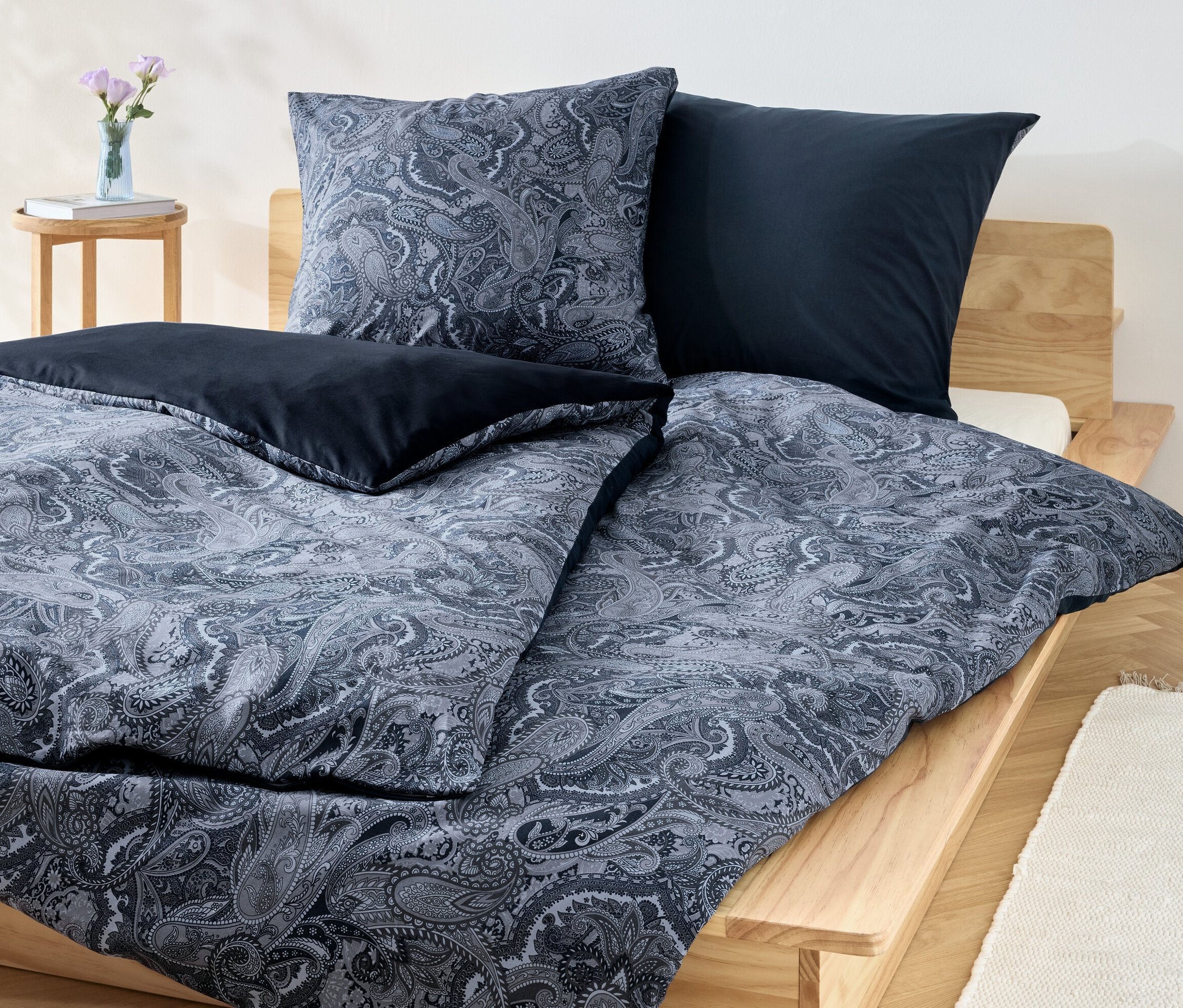 Niebieski komplet pościeli z bawełny renforcé we wzory kwiatowe i jednolite niebieskie poduszki na drewnianym łóżku.