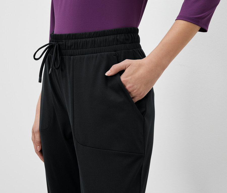 Częściowy widok osoby w czarnych spodniach dresowych z ręką w kieszeni.