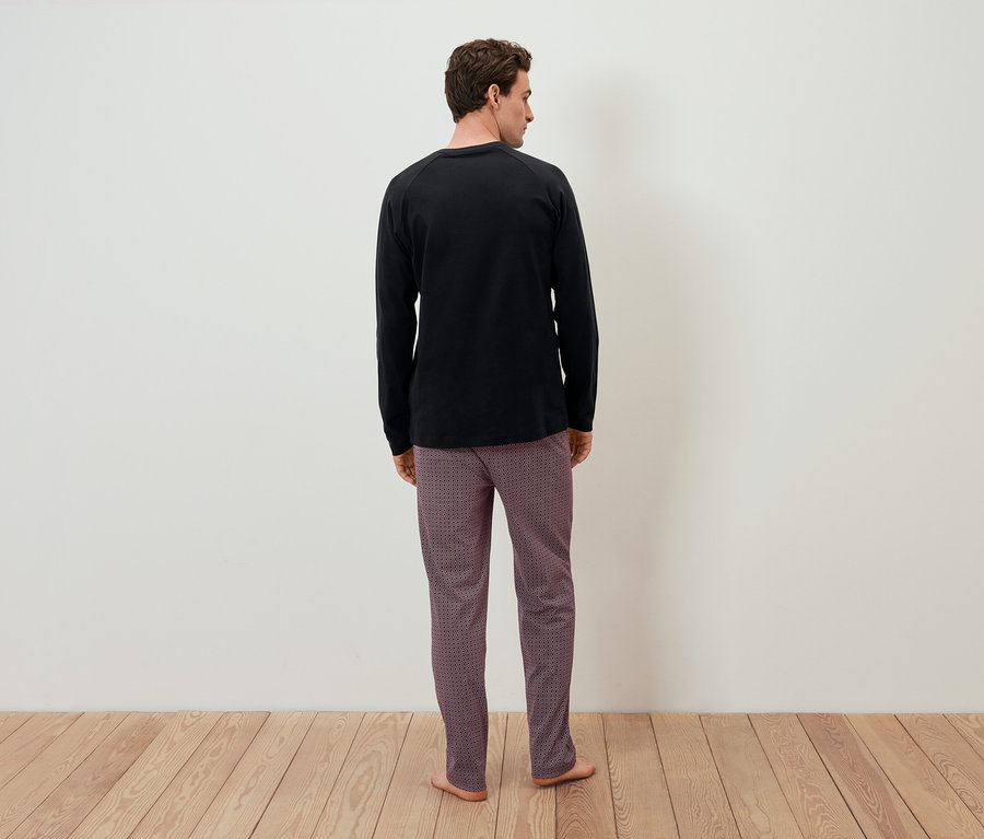 Mężczyzna tyłem do kamery w czarnej koszulce z długim rękawem i wzorzystych spodniach.