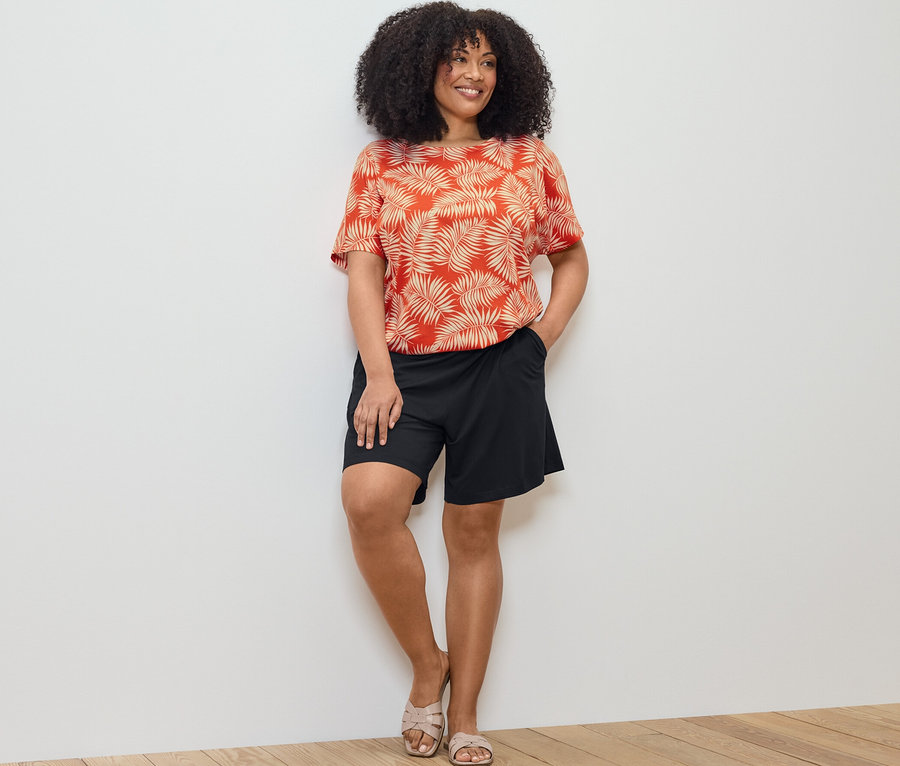 Kobieta pozuje w wzorzystej bluzce i czarnych szortach z dżerseju.