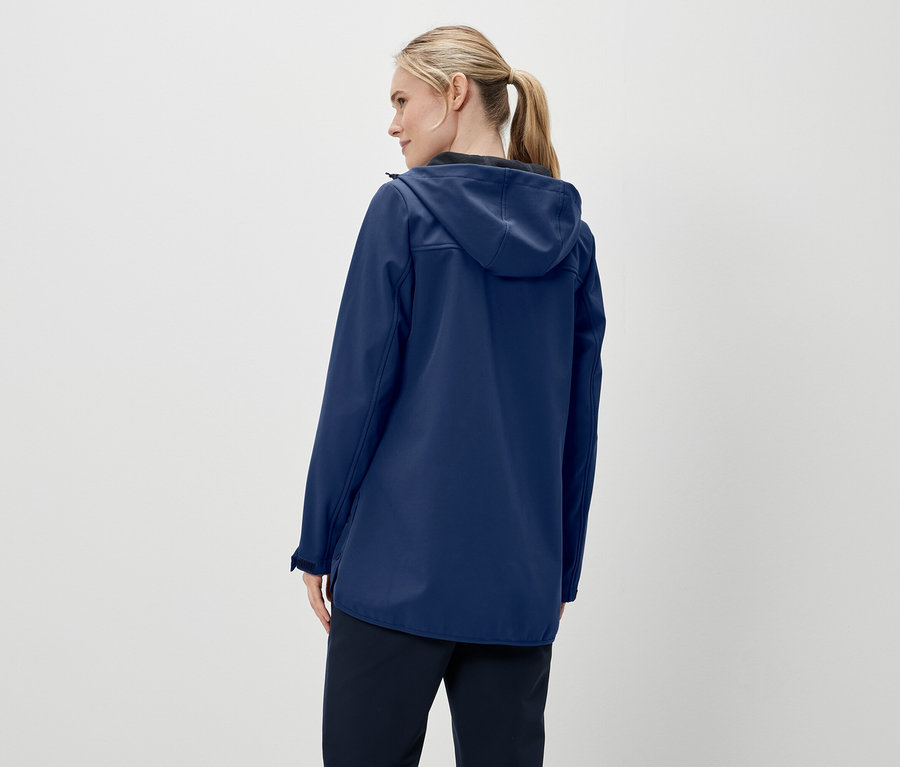 Widok z tyłu na kobietę z blond włosami związanymi w kucyk, ubraną w granatową kurtkę z kapturem i ciemne spodnie.