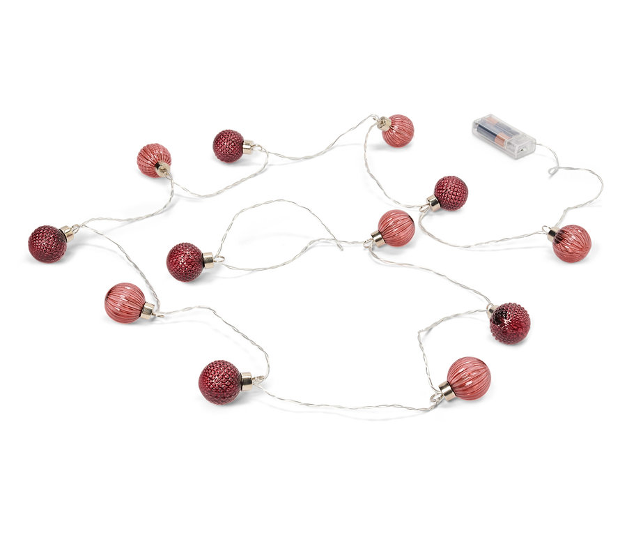 Na białym tle leży łańcuch światełek z czerwonymi bombkami i bateriami.