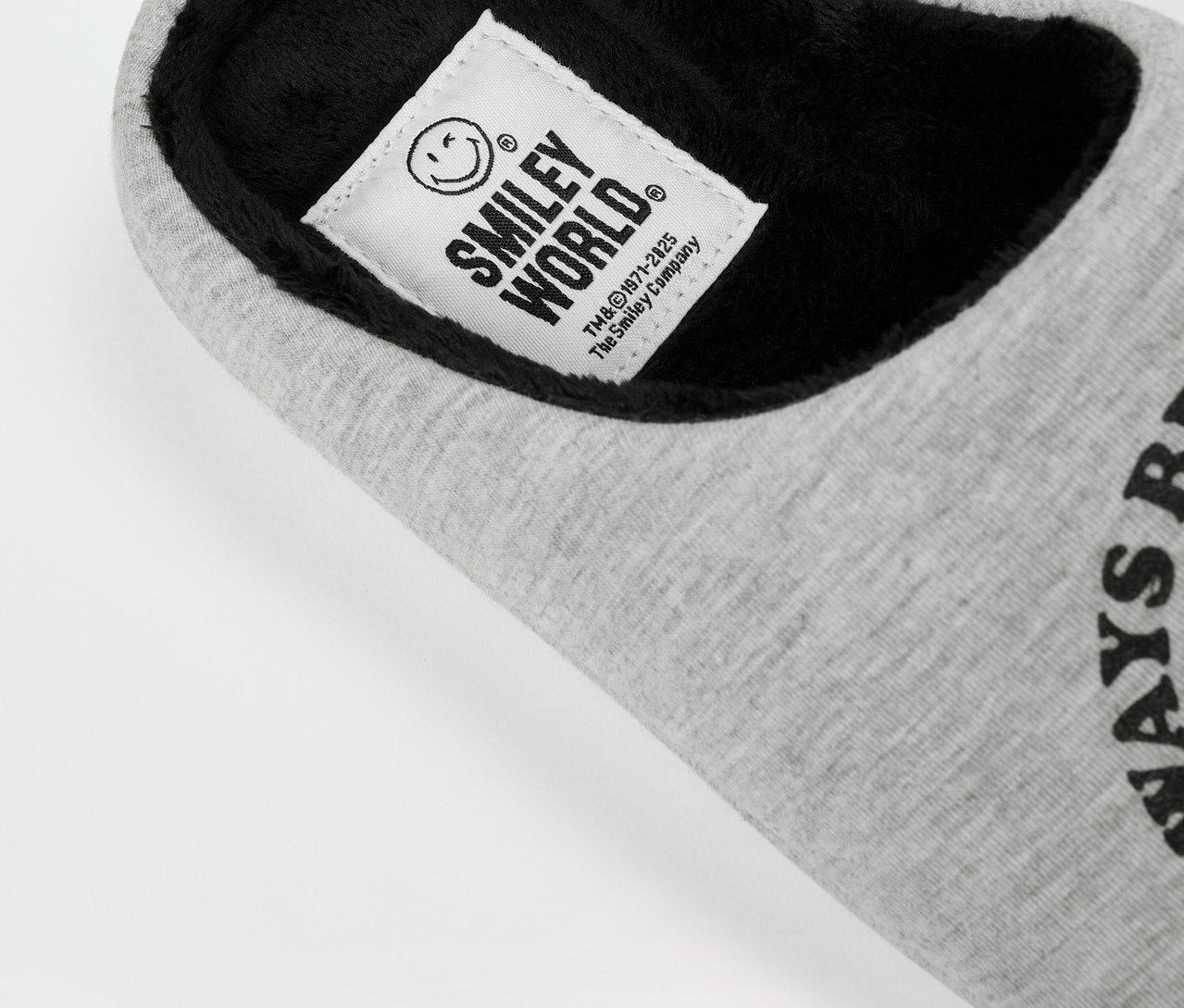 Zbliżenie szarego, tekstylnego kapcia SMILEYWORLD® z czarną wyściółką wewnętrzną i etykietą z logo.
