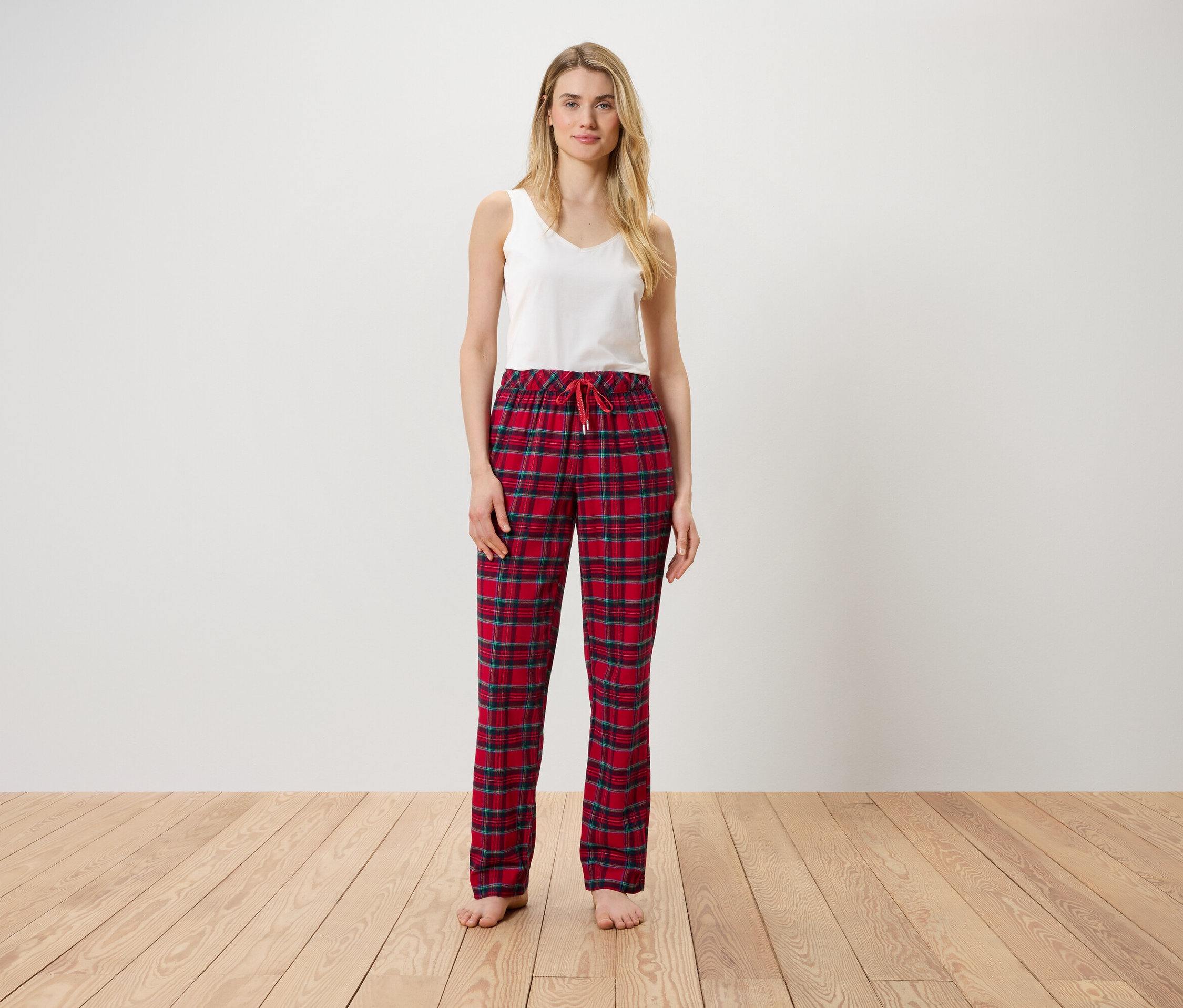 Kobieta stoi, ubrana w biały top i czerwone spodnie w kratę.