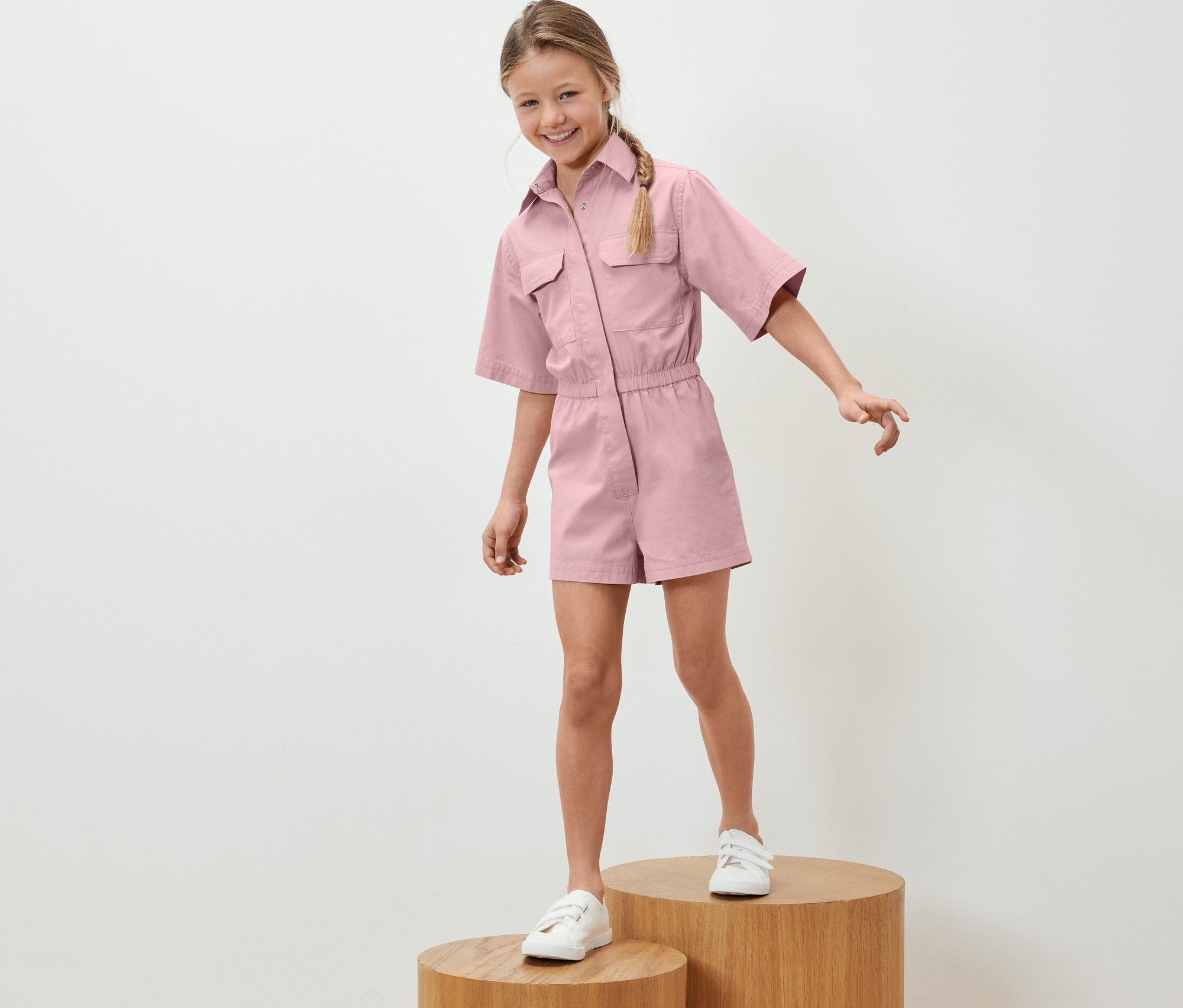 Dziewczynka stoi na drewnianych podstawkach i ma na sobie kombinezon.