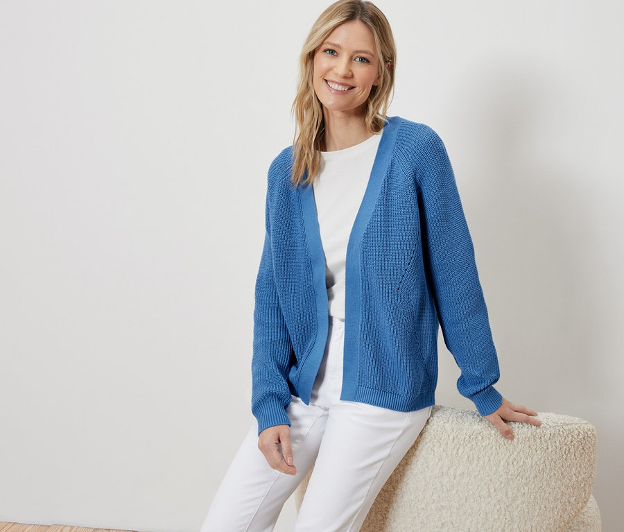 Kobieta siedzi i ma na sobie niebieski kardigan.