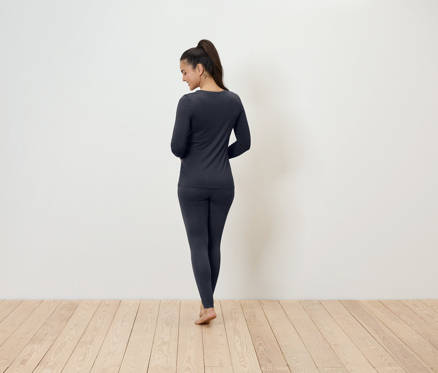 Kobieta stoi tyłem do aparatu, ubrana w ciemnoszarą bieliznę termiczną.