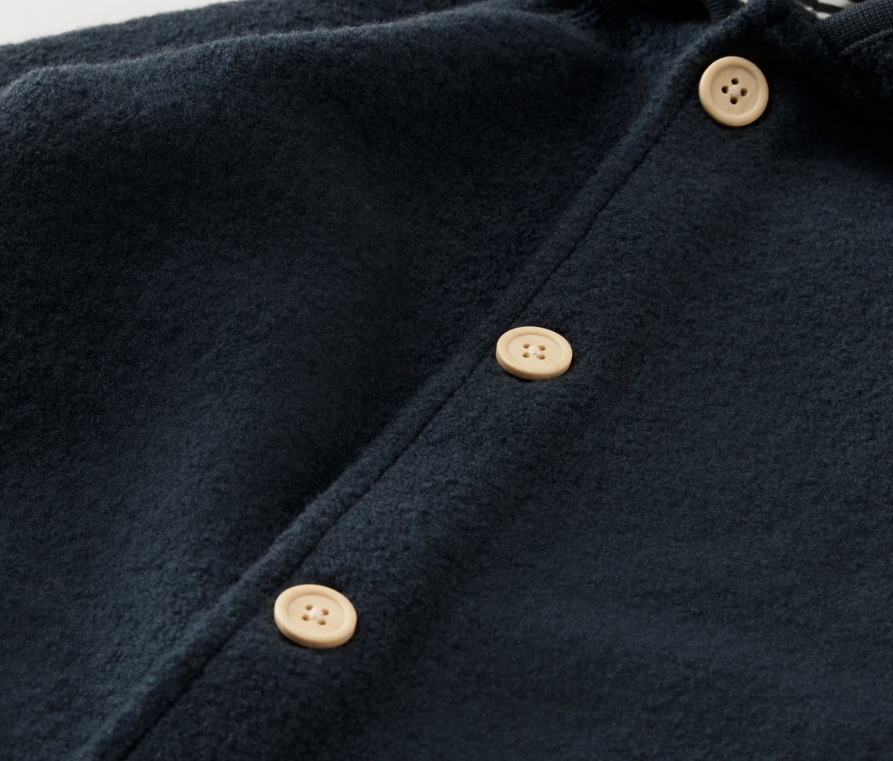 Szczegół granatowego kombinezonu dziecięcego z wełny merino z jasnymi guzikami.