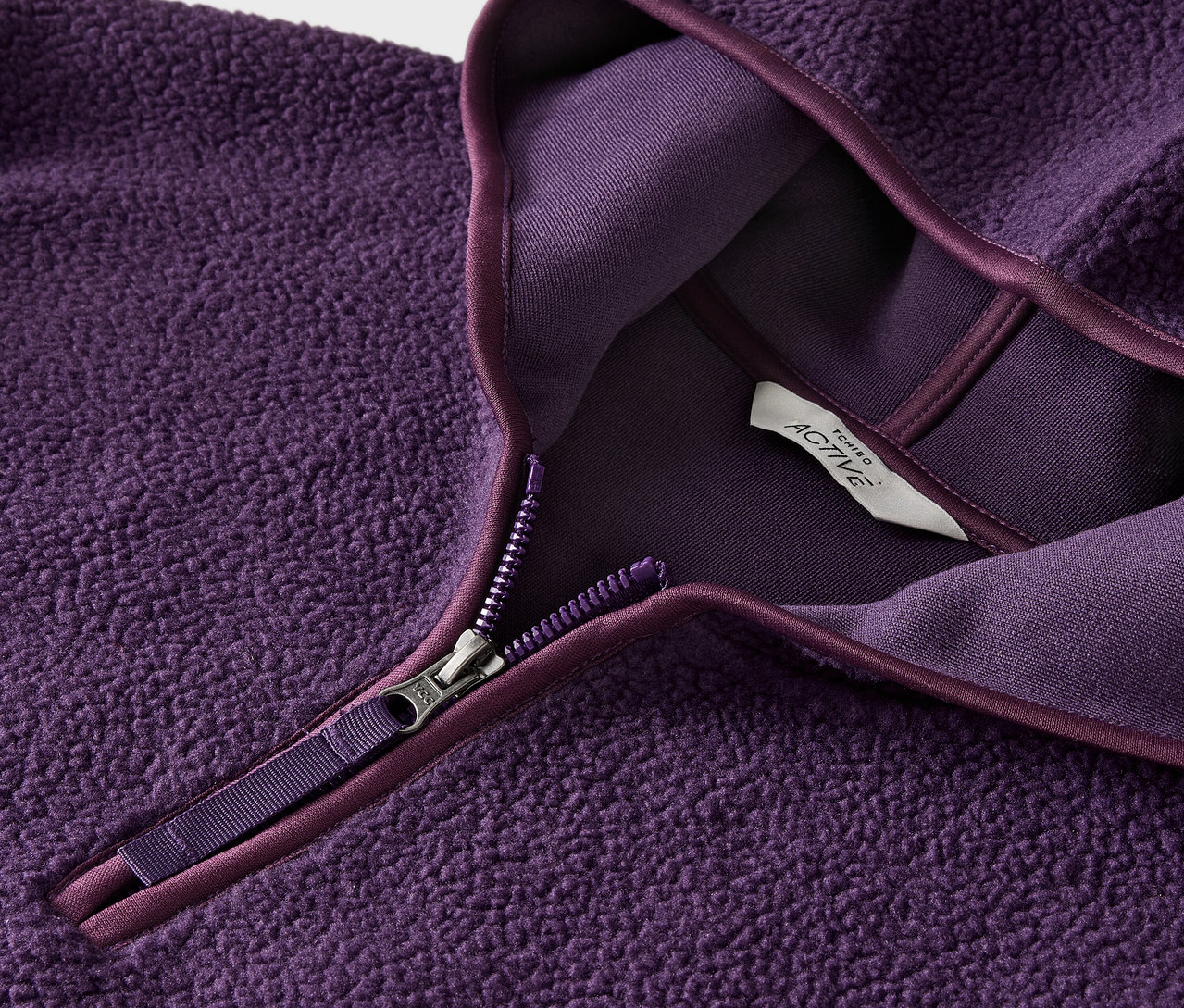 Zbliżenie fioletowej bluzy polarowej z zamkiem błyskawicznym i metką.