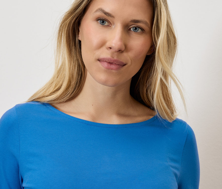 Portret blondynki w niebieskiej bluzce z długim rękawem.
