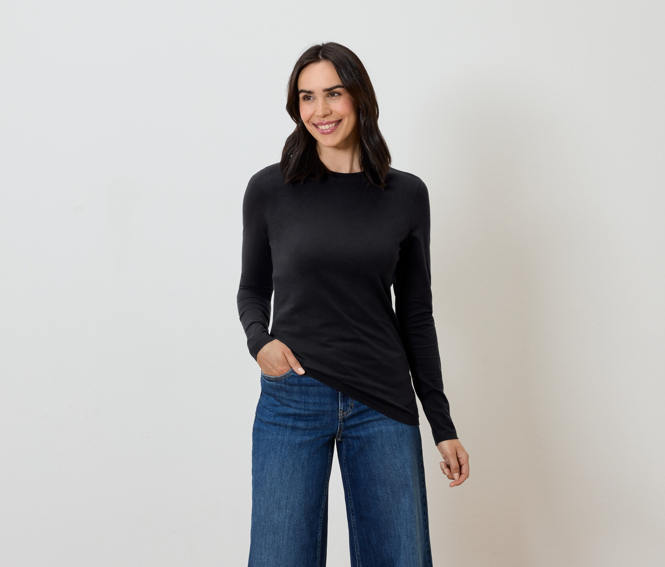 Kobieta z brązowymi włosami pozuje w czarnej bluzce z długim rękawem i niebieskich dżinsach.