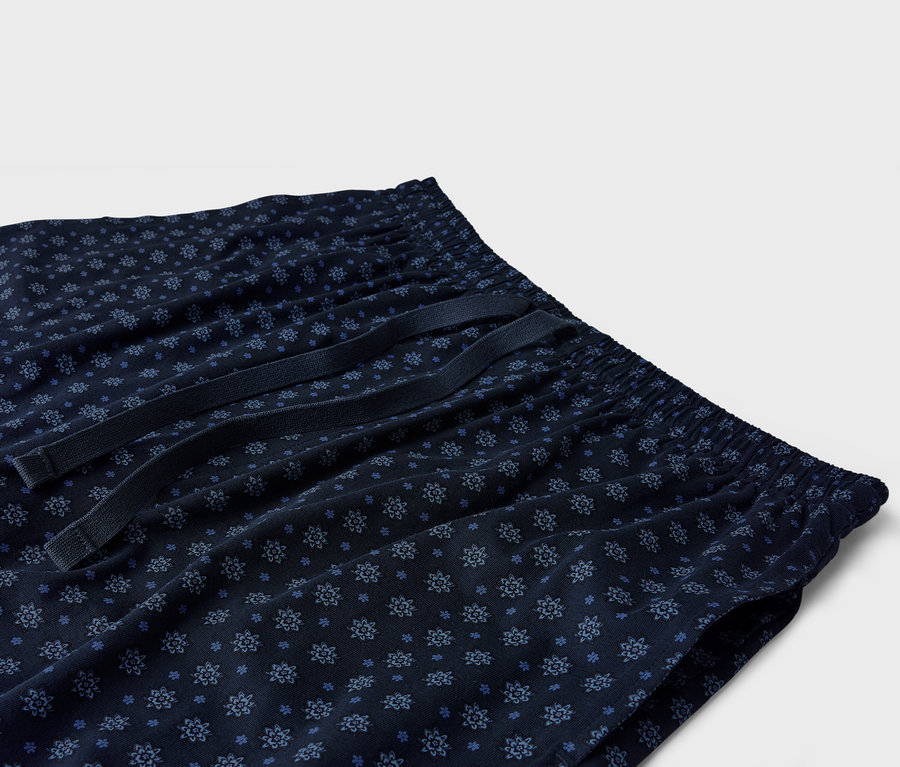 Zbliżenie granatowych spodni od piżamy z niebieskim kwiatowym wzorem i sznurkiem.